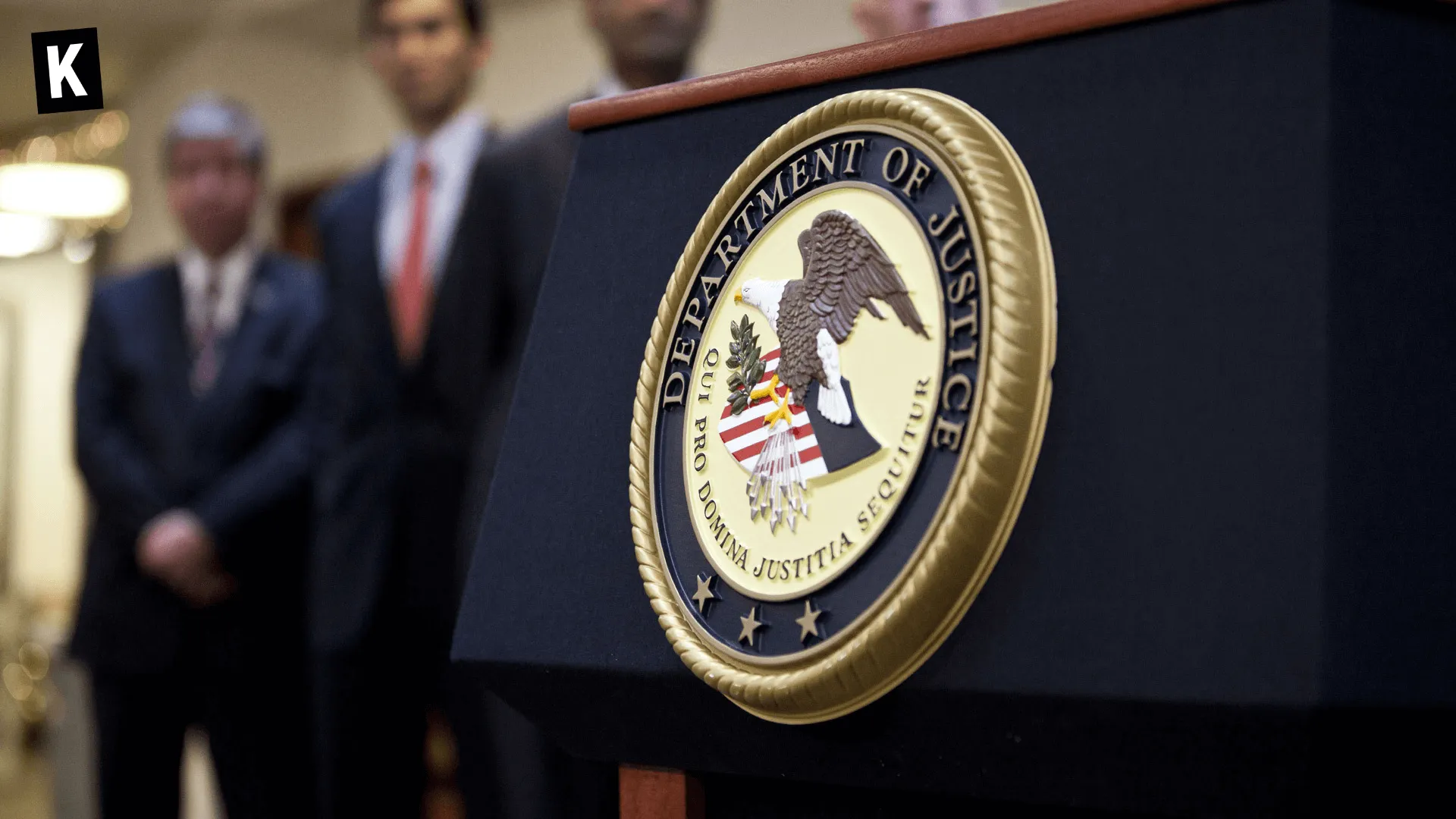 Seal of the U.S. Department of Justice on a lectern with officials in the background